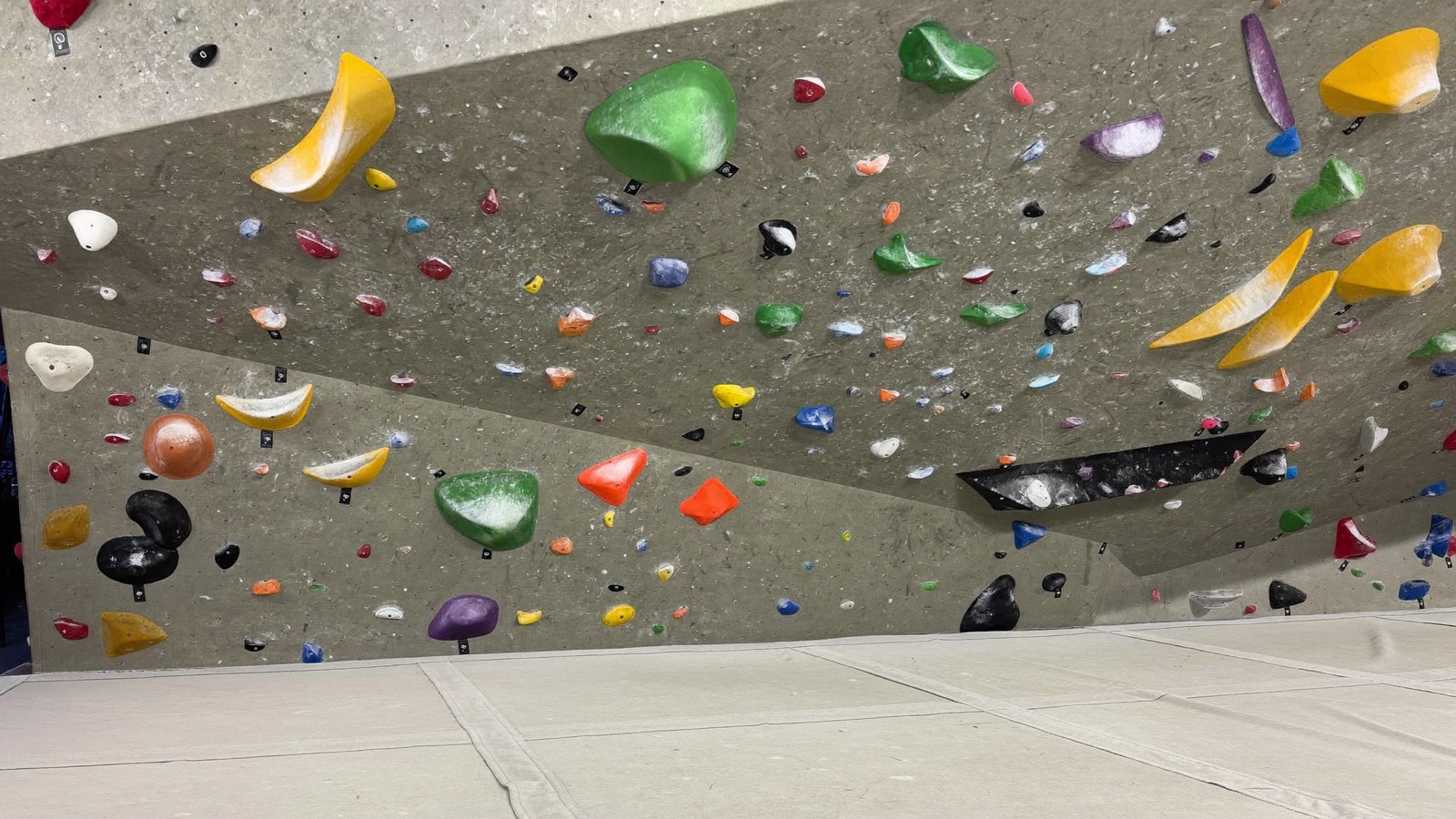 Climbers working colorful taped problems on Overhang's steep 45 degree bouldering wall after a fresh reset, holds running top to bottom.